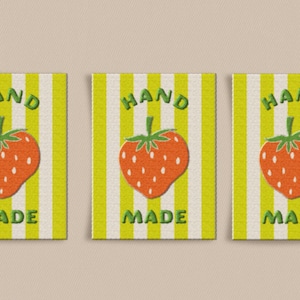 May include: Three rectangular fabric labels with a yellow and white striped background. Each label features a red strawberry illustration and the words "HAND MADE" in green letters.