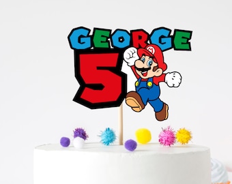 May include: A cake topper featuring a cartoon image of Mario from the Super Mario Bros. video game. The topper includes the name "GEORGE" in blue and green letters, the number "5" in red, and colorful pom-poms.