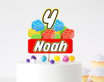 May include: A red, white, and yellow Lego-themed cake topper with the number 4 and the name Noah. The topper is on a white cake with colorful pom-poms around the base.