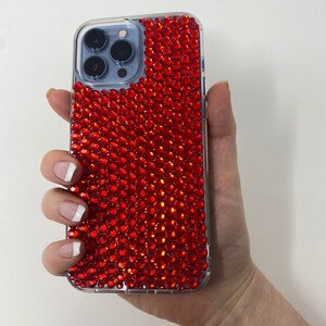 May include: A clear phone case with a red rhinestone design. The case is designed for an iPhone.