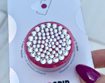May include: A pink PopGrip phone grip with a clear, sparkly, diamond-like design. The grip is packaged in a white box with the words "PopSockets" and "PopGrip Premium" printed on it.