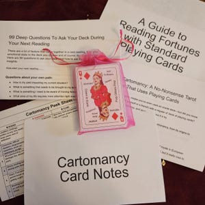 May include: A deck of cartomancy cards in a pink organza bag, with accompanying notes and guides. The cards feature a red and white illustration of a queen. Text on the cards includes "Stressed", "Sensible", and "Down to Earth".