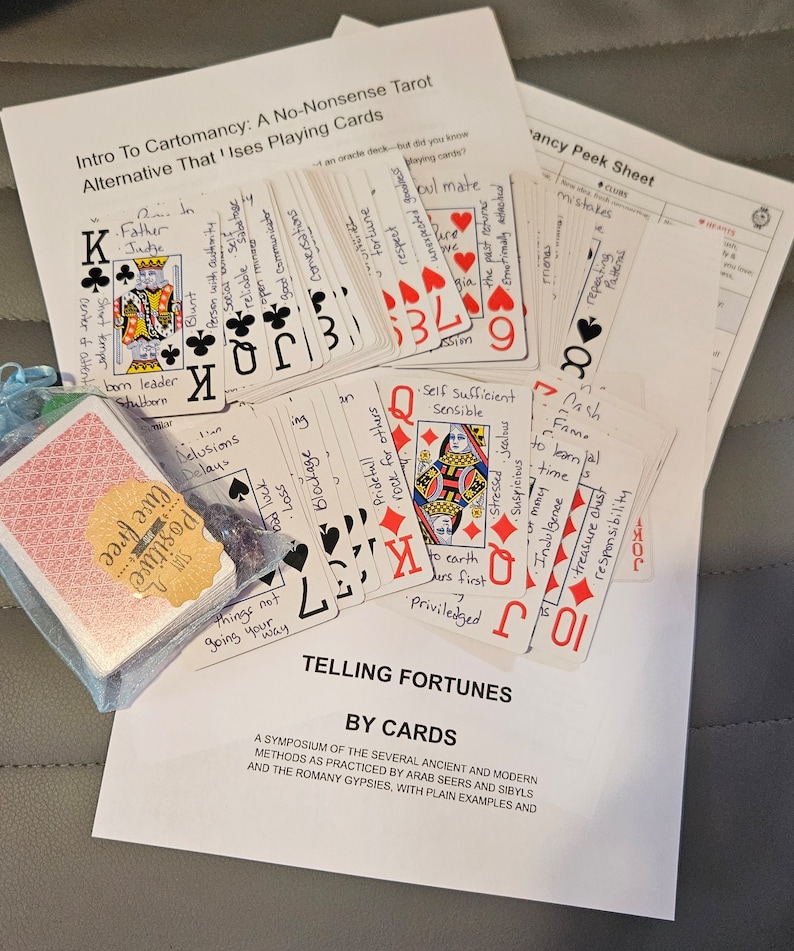 May include: A close-up of a stack of playing cards with handwritten text on each card. The text includes words like 'father', 'judge', 'self sufficient', 'sensible', 'cash', 'fame', 'to learn', 'time', 'treasure chest', 'responsibility', 'blockage', 'rock for others', 'pridefull', 'delusions', 'delay', 'things not going your way', 'positive', 'hope live free', 'stubborn', 'born leader', 'short temper', 'center of attention', 'temps', 'good communicator', 'open mindes', 'social', 'person with authority', 'the past returns', 'emotionally attached', 'patterns', 'stressed jealous', 'suspicious of money', 'indulgence', 'to earth', 'ders first', 'privileged', 'pul mate', 'unexpected goodness', 'fortune', 'respect', 'bad luck', 'we', 'bia', 'sion'. The cards are arranged in a stack with the top card facing up. The cards are on a white surface. The text 'Telling Fortunes By Cards' is printed on the white surface. The text below reads 'A symposium of the several ancient and modern methods as practiced by Arab seers and sibyls and the Romany gypsies, with plain examples and'