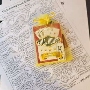 May include: A red and white playing card with a black 'K' for King on it. The card is in a yellow mesh bag with the words 'Full House' printed on it. The card is on top of a white sheet of paper with black ink drawings of swirling lines and words. The words on the paper include 'Diamond', 'Clubs', 'Hearts', 'New opportunity', 'Brand new', 'New life', 'Fresh start', 'Breaking away', 'Letting go', 'Deception', 'Delusions', 'Sadness', 'Serious', 'Fear & worry', 'Tomfoolery', 'Clever, acts quickly', 'Quick wit', 'Let them charge', 'Curious, busy and fearless', 'Charming, dominance', 'Popular', 'Business', 'Peaceful home', 'Long term', 'Generous', 'Joy', 'Heart, sentimental', 'Spoiled, passive', 'Daydream', 'Too giving', 'Moody', 'Past', 'Someone from the past', 'Identity from the past', 'Significant if identity made', 'Mature man, significant & influential', 'Mature woman', 'Mature man'