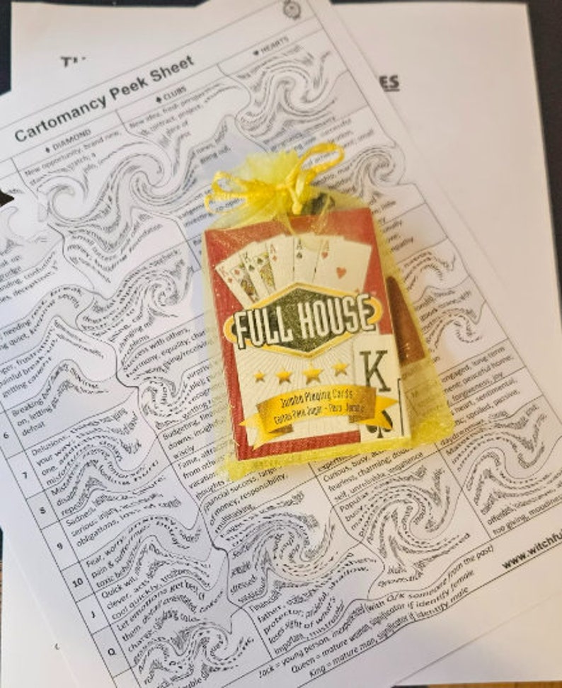 May include: A red and white playing card with a black 'K' for King on it. The card is in a yellow mesh bag with the words 'Full House' printed on it. The card is on top of a white sheet of paper with black ink drawings of swirling lines and words. The words on the paper include 'Diamond', 'Clubs', 'Hearts', 'New opportunity', 'Brand new', 'New life', 'Fresh start', 'Breaking away', 'Letting go', 'Deception', 'Delusions', 'Sadness', 'Serious', 'Fear & worry', 'Tomfoolery', 'Clever, acts quickly', 'Quick wit', 'Let them charge', 'Curious, busy and fearless', 'Charming, dominance', 'Popular', 'Business', 'Peaceful home', 'Long term', 'Generous', 'Joy', 'Heart, sentimental', 'Spoiled, passive', 'Daydream', 'Too giving', 'Moody', 'Past', 'Someone from the past', 'Identity from the past', 'Significant if identity made', 'Mature man, significant & influential', 'Mature woman', 'Mature man'