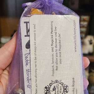 May include: A purple mesh bag with a white card inside. The card has the text 'Witchful Ways' and 'Products, Services, and Magickal Mentoring that allow you to discover and live your most Magickal Life!' The card also has the text 'www.witchfulways.com' and 'Annika Rogue Owner'.