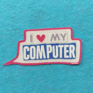Peut inclure: Un autocollant blanc et bleu en forme de bulle de dialogue avec le texte "I ♥ MY COMPUTER". Le texte est en bleu, avec un symbole de cœur rouge. L'autocollant a une bordure rose et est sur un fond bleu.