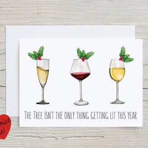 May include: A white greeting card with three wine glasses, each topped with holly. The glasses contain champagne, red wine, and white wine. The text reads, "The Tree Isn't the Only Thing Getting Lit This Year."