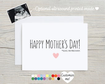 May include: A white card with black text that reads "Happy Mother's Day! *ALSO, I'M PREGNANT." A pink heart is below the text. The card is on a woodgrain background.