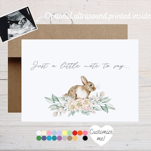 May include: A white card with the text "Just a little note to say..." and a watercolor illustration of a brown bunny sitting on a bed of pink flowers and green leaves. The card is surrounded by a brown envelope.