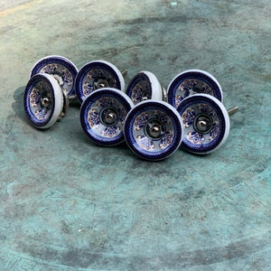 May include: Eight ceramic drawer knobs with a blue and white floral pattern and gold accents. The knobs have a silver metal base.