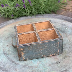 May include: A small wooden box with four compartments. The box is painted a faded blue colour and has a handle on the side. The box is sitting on a silver tray.