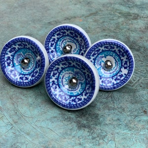 May include: Four ceramic drawer knobs with a blue and white patterned design. Each knob has a silver metal centre.