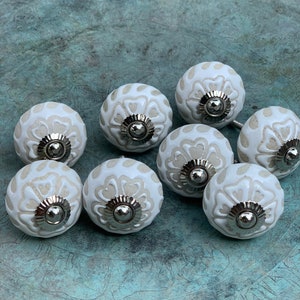 May include: Eight white ceramic cabinet knobs with a silver metal base and a floral design.