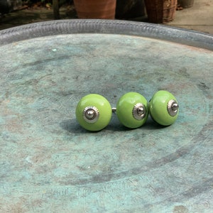 May include: Three green ceramic cabinet knobs with silver accents. The knobs are arranged in a row on a silver tray.