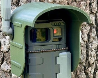 May include: A green camouflage trail camera with a black lens and a red LED light. The camera is mounted on a tree and has a green protective cover.