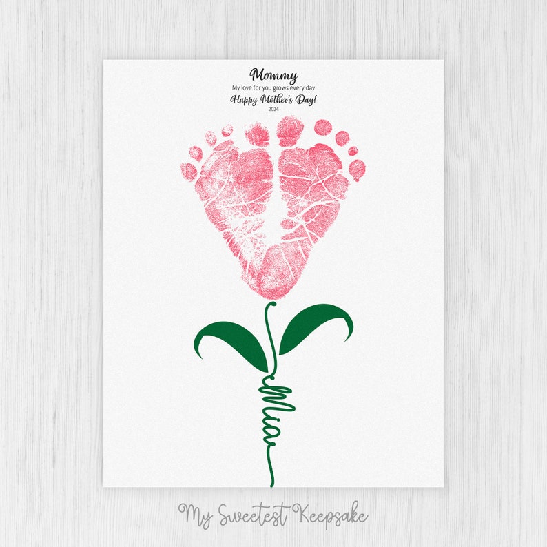 Op de afbeelding: Een roze voet afdruk bloem met groene bladeren en een stengel waarop "Mommy" in cursief staat. De tekst boven de bloem luidt "My love for you grows every day Happy Mother's Day!" en de tekst onder de bloem luidt "My Sweetest Keepsake".