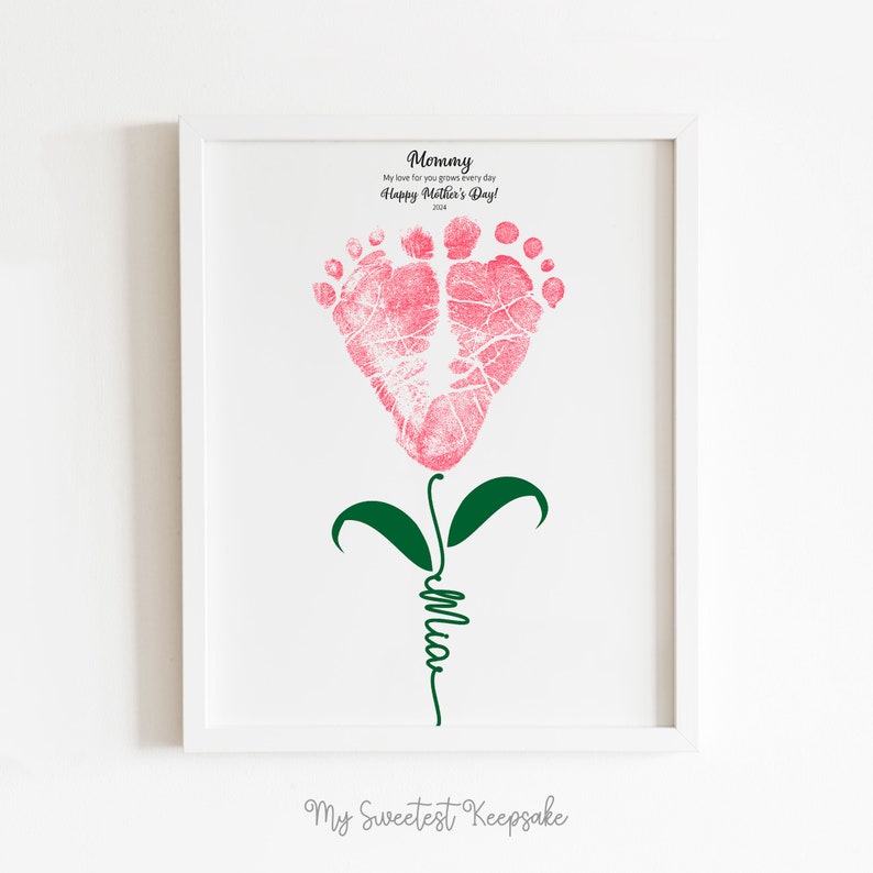 Op de afbeelding: Een roze voet afdruk bloem met groene bladeren en een stengel waarop "Mommy" in cursief staat. De tekst boven de bloem luidt "My love for you grows every day Happy Mother's Day!" en de tekst onder de bloem luidt "My Sweetest Keepsake".