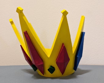 May include: A yellow crown with red, blue, and green gems. The crown is made of foam and is painted yellow. The gems are painted red, blue, and green.