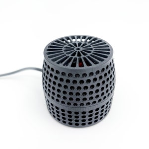May include: A black, cylindrical, 3D printed fan with a circular, open-grid design on the top and bottom. The fan has a red centre and a black cord.