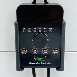 Puede incluir: Controlador de generador de olas negro con un dial y botones etiquetados "WI-LI FEED", "FLOW LIGHT", "WAVE MODE" y "TIME MODE". El controlador tiene un logotipo "hygger" verde y el texto "Wavemaker Controller".