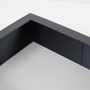 May include: A dark gray rectangular frame with a white background. The frame is made of a thick, sturdy material and has a smooth finish.