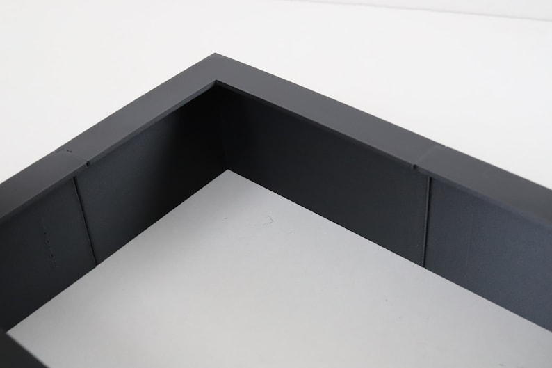 May include: A dark gray rectangular frame with a white background. The frame is made of a thick, sturdy material and has a smooth finish.