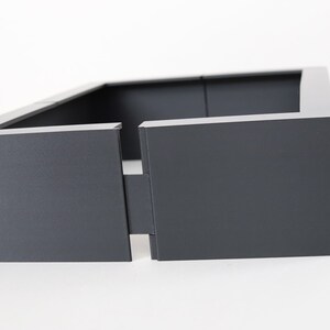 May include: A dark gray rectangular planter with a square opening in the front. The planter is made of a sturdy material and has a modern design.