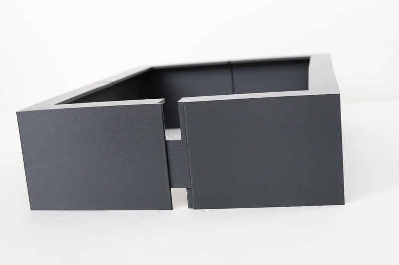 May include: A dark gray rectangular planter with a square opening in the front. The planter is made of a sturdy material and has a modern design.