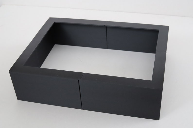 May include: A black metal fire pit frame with a square shape. The frame is made of four pieces that fit together to create a square.