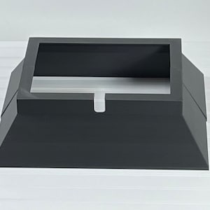 May include: A black metal chimney cap with a square base and a rectangular opening. The cap has a small lip around the opening.
