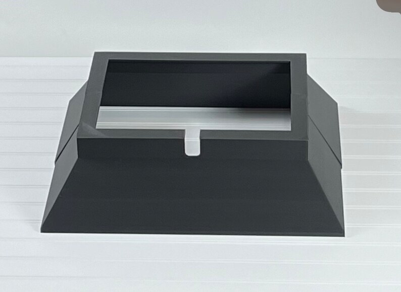May include: A black metal chimney cap with a square base and a rectangular opening. The cap has a small lip around the opening.