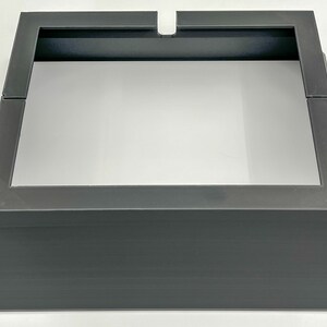 May include: A black metal stand with a square top and a raised base. The stand is designed to hold a square object, such as a speaker or a plant.