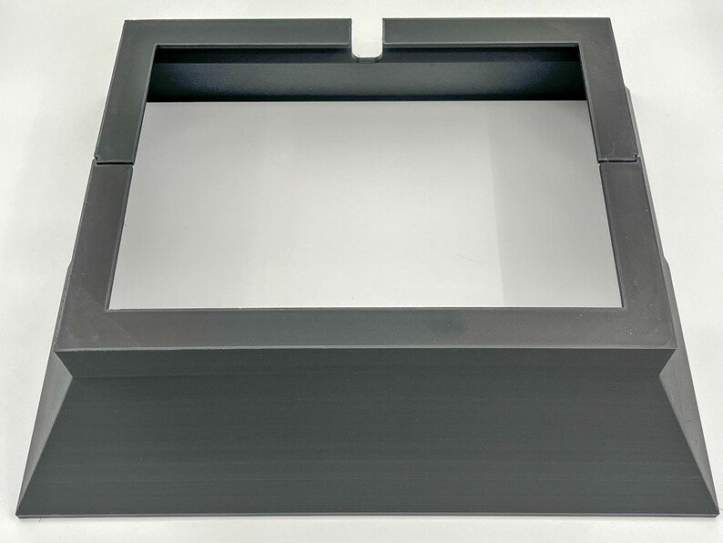 May include: A black metal stand with a square top and a raised base. The stand is designed to hold a square object, such as a speaker or a plant.