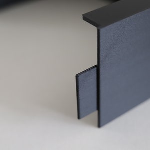 May include: Close-up of a black plastic storage box with a textured surface. The box has a removable lid and a small, black plastic tab on the side.