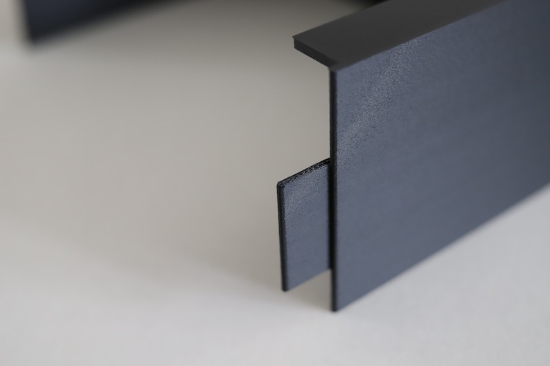 May include: Close-up of a black plastic storage box with a textured surface. The box has a removable lid and a small, black plastic tab on the side.