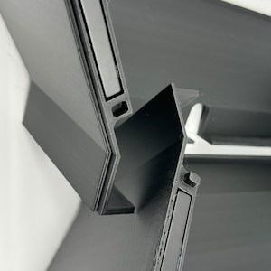 May include: Two black plastic pieces with a rectangular magnet embedded in each piece. The pieces are designed to connect together.