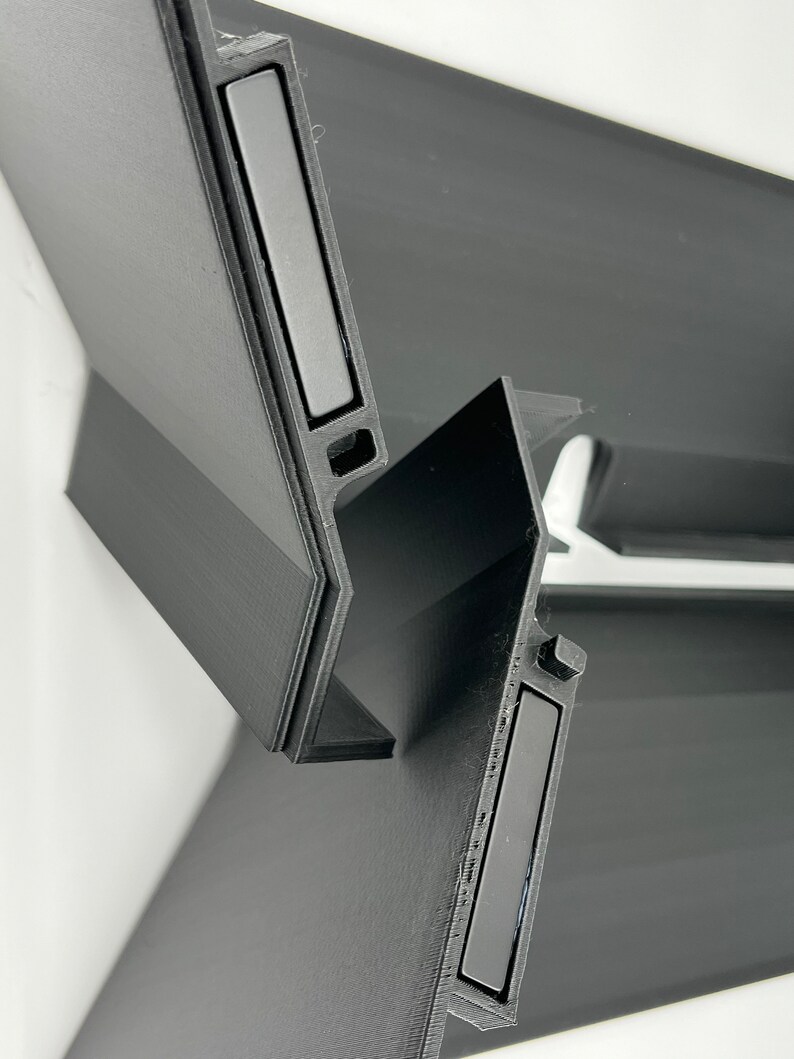 May include: Two black plastic pieces with a rectangular magnet embedded in each piece. The pieces are designed to connect together.