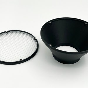 Può includere: Un diffusore a nido d'ape nero per flash o luce da studio. Il diffusore è in plastica e ha una cornice in metallo nero. Il diffusore è progettato per ammorbidire la luce e creare una diffusione più uniforme.