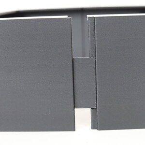 May include: Close-up of a gray, rectangular box with a hinge in the middle. The box is made of a sturdy material and has a smooth, matte finish.