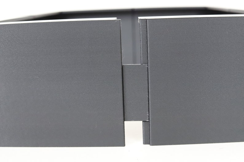May include: Close-up of a gray, rectangular box with a hinge in the middle. The box is made of a sturdy material and has a smooth, matte finish.