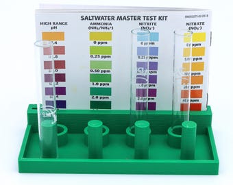 May include: A green plastic test tube rack with four clear glass test tubes. The rack has a white card attached to it with the words "Saltwater Master Test Kit" and the labels "Ammonia (NH3/NH4+)", "Nitrite (NO2)", and "Nitrate (NO3)". The card has a color chart for each test with measurements in parts per million (ppm).