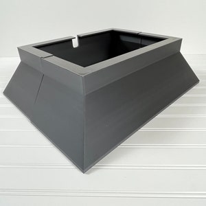 May include: A gray metal tree stand with a square base and a rectangular top. The stand is designed to hold a Christmas tree.