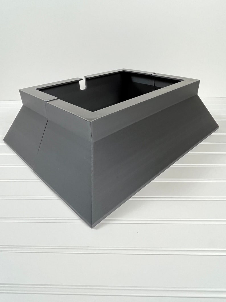 May include: A gray metal tree stand with a square base and a rectangular top. The stand is designed to hold a Christmas tree.