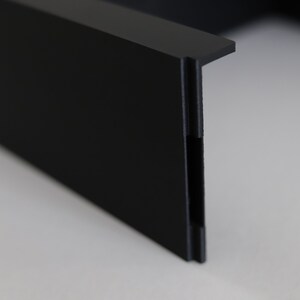 May include: Close-up of a black plastic corner piece with a smooth, matte finish. The corner piece has a slight curve and a small lip on the top edge.
