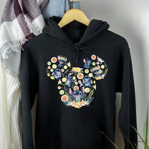 K&ouml;nnte beinhalten: Schwarzer Kapuzenpullover mit einem bunten Motiv von Stitch-Charakteren in Form eines Mickey-Maus-Kopfes. Das Motiv zeigt Stitch-Charaktere mit Blumen und Zitronen.