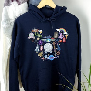 May include: A navy blue hoodie featuring a white graphic print of a Mickey Mouse head filled with various Disney park icons, including Spaceship Earth, Cinderella's Castle, and a rainbow.