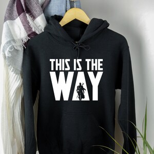 May include: Black hooded sweatshirt with white text that reads "This is the Way" and a silhouette of a figure in a Mandalorian helmet and armour.