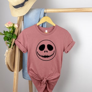 May include: A mauve t-shirt with a black Jack Skellington face graphic.