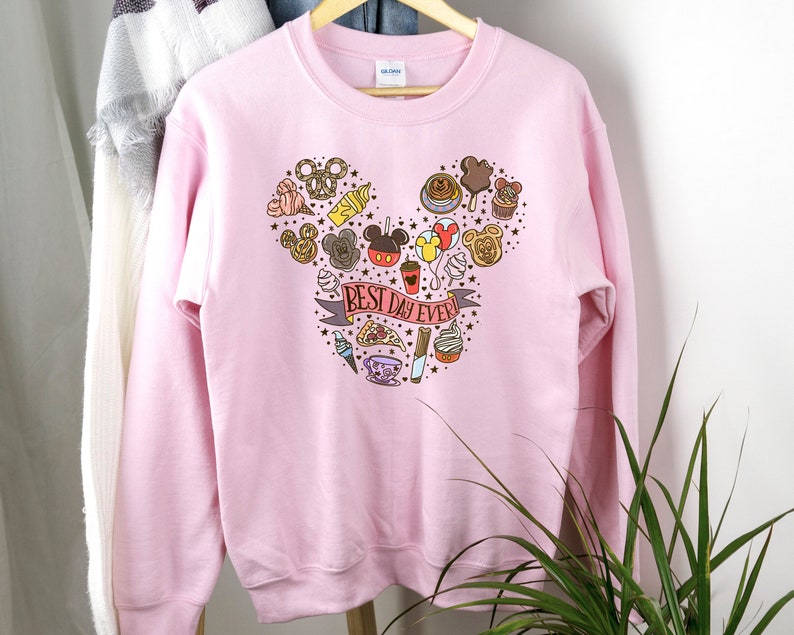 May include: Pink sweatshirt with a Mickey Mouse head design made up of various Disney-themed icons and the text "BEST DAY EVER!" printed on the front.